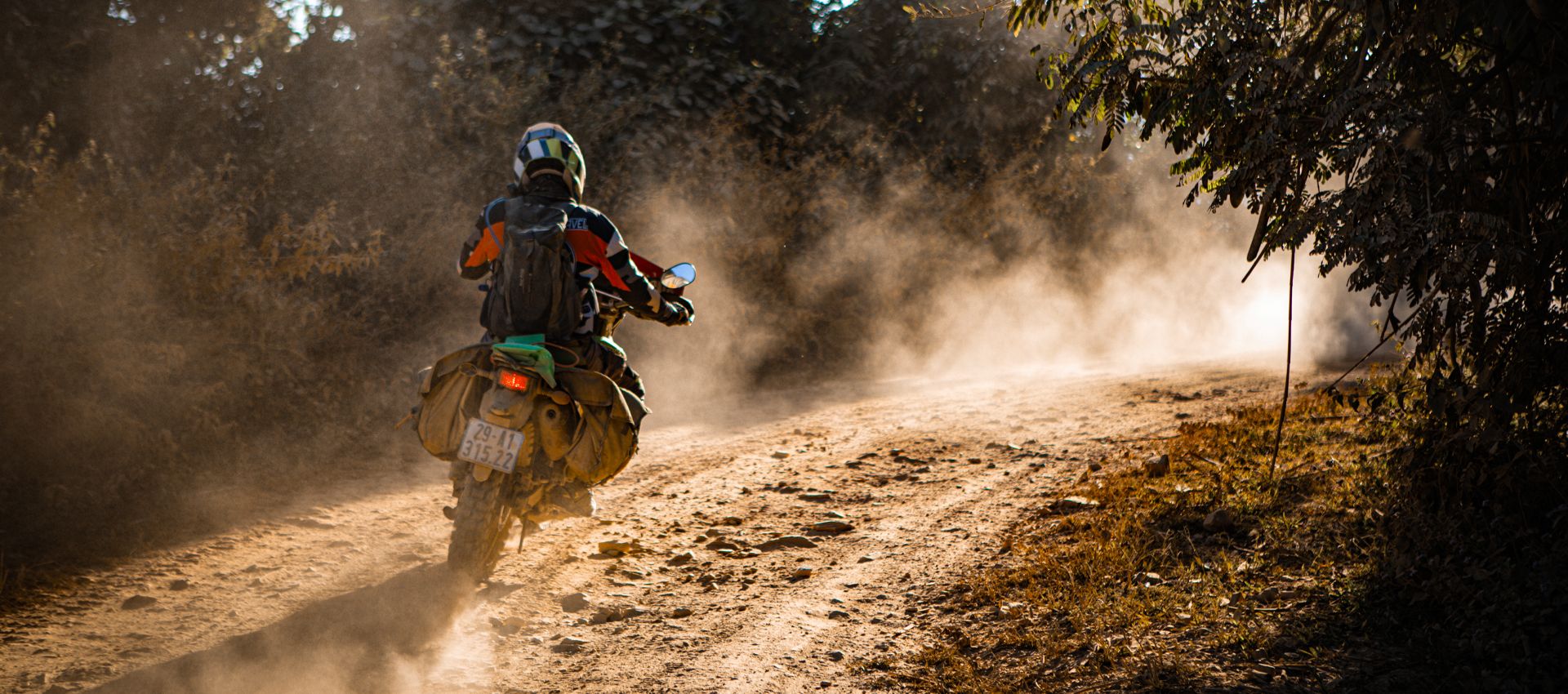 Motorcyclist riding on a dusty dirt road with dust clouds trailing behind in golden light